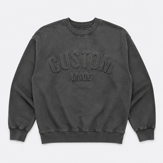 A dark gray washed crewneck sweatshirt with 'CUSTOM MADE' embossed on the chest, displayed flat against a light gray background.
