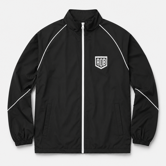 A black zip-up windbreaker jacket with white piping details and a white shield logo on the left chest, displayed on a light gray background.