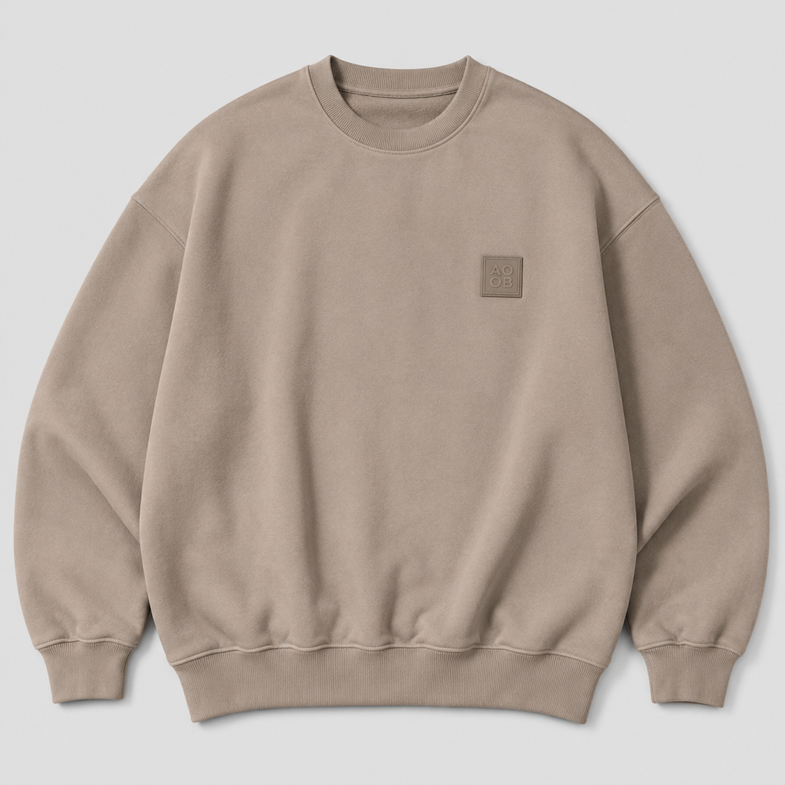 A taupe crewneck sweatshirt with a small tonal square patch on the left chest, displayed flat against a light gray background.